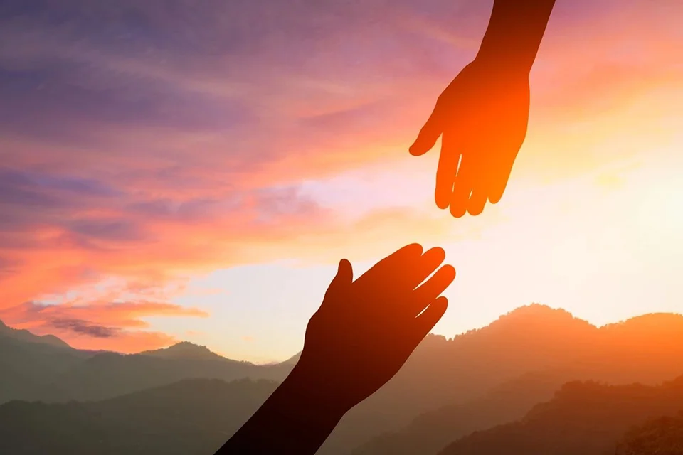 Two hands reaching out towards each other in the sunset.