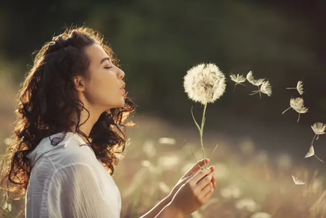 A woman holding a dandelion in her hand.