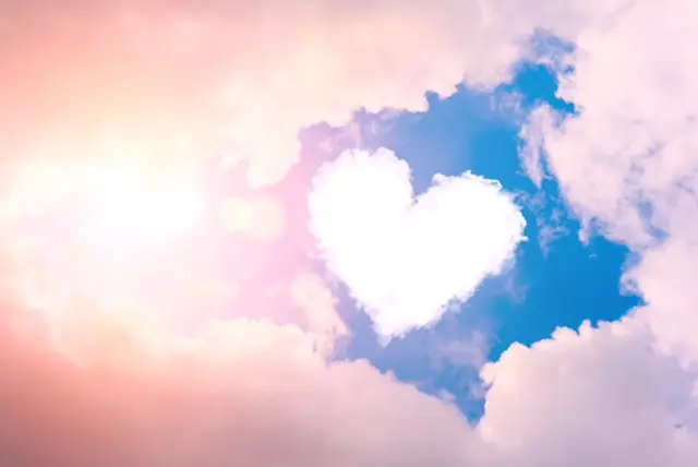 A heart shaped cloud in the sky with sun shining